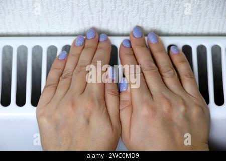 Les mains féminines sur le radiateur de chauffage. Hiver temps froid, saison de chauffage à la maison Banque D'Images