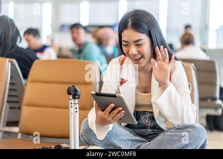 Une jeune femme asiatique en appel vidéo sur sa tablette au terminal de l'aéroport Banque D'Images