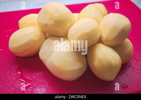 Tubercules de pomme de terre pelés sur une planche à découper rouge. Banque D'Images