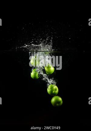Prune verte tombait dans l'eau avec des bulles isolées sur un fond noir. Banque D'Images