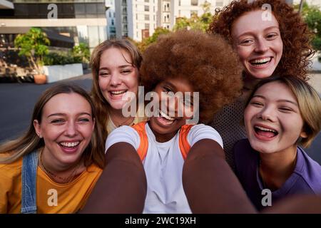 Heureux amis féminins multiraciaux prenant un selfie avec un smartphone à l'extérieur. Banque D'Images