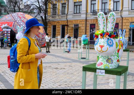 Fille souriante regardant une installation de lapin peinte comme un œuf de Pâques dans une rue. Festival d'art folklorique 18 avril 2018. Kiev, Ukraine Banque D'Images