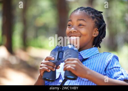 Binoculaire, recherche ou enfant garçon heureux dans la randonnée en forêt, le tourisme ou la découverte. Objectif, équipement ou enfant africain excité dans la nature pour l'aventure Banque D'Images