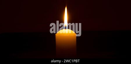 La flamme ou la lumière de bougie brûlante unique brille sur une grande bougie blanche sur fond noir ou sombre sur la table dans l'église pour Noël, funérailles Banque D'Images