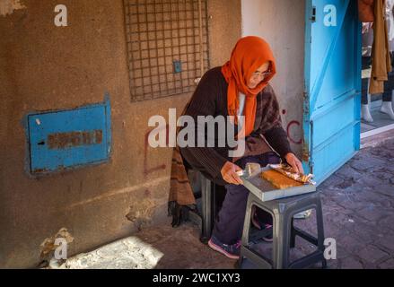 Une femme tunisienne âgée vend des gâteaux faits maison dans une petite ruelle à l'intérieur de l'ancienne médina fortifiée de Sousse en Tunisie. Banque D'Images