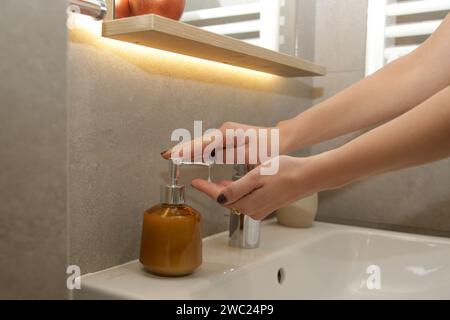 Femme se lavant les mains en utilisant du savon sous l'eau dans l'évier de salle de bain Banque D'Images