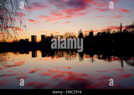 Crépuscule dans le parc Herastrau à Bucarest, Roumanie, avec des nuages rouges sur le ciel bleu reflétés sur l'eau du lac Banque D'Images