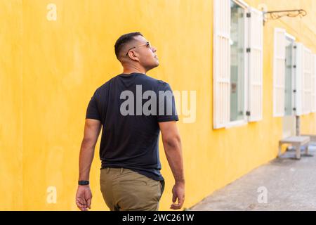 Homme en t-shirt noir regarde loin avec réflexion, fond jaune vif mur. Banque D'Images