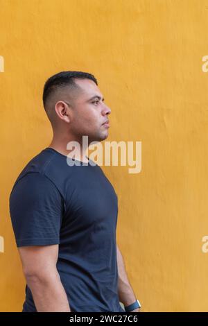 Un homme pensif dans un t-shirt sombre se dresse sur un fond jaune Uni, offrant une vue de profil. Banque D'Images