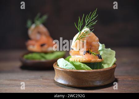 Collation de fête à partir de crevettes, saumon, caviar et aneth garniture dans de petits bols en bois sur une table rustique sombre, apéritif pour des vacances comme Noël, Thanksgi Banque D'Images