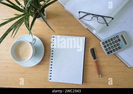 Maquette de bloc-notes en spirale vierge sur un bureau avec dossier, calculatrice, tasse à café et une usine, concept pour la comptabilité des affaires et des finances, angle élevé Banque D'Images