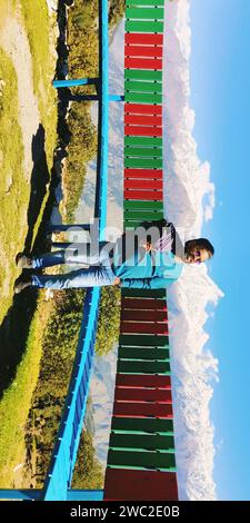 Une femme adulte se tient debout sur une rangée de bancs multicolores surplombant un paysage marin Banque D'Images