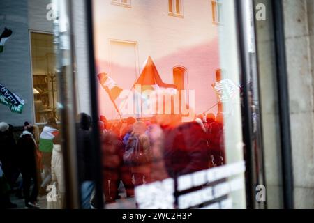 Spiegelung der Demo im Schaufenster. AM 13.01.2024 versammelten sich erneut Hunderte Menschen, UM für einen sofortigen Waffenstillstand im sog. Nah-Ost-Konflikt zu demonstrieren und UM ihre Solidarität mit Palästina zu zeigen. SIE trauerten UM die Toten in Palästina und forderten Frieden für Gaza und einen Stopp des Krieges. -- réflexion de la démo dans une vitrine. Le 13 janvier 2024, des centaines de personnes se sont rassemblées à Munich, en Allemagne, pour protester pour un cessez-le-feu immédiat au Moyen-Orient et pour montrer leur solidarité avec les Palestiniens. Ils ont pleuré les victimes en Palestine, appelé à la paix pour gaz Banque D'Images