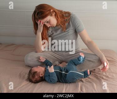 Une femme caucasienne est assise sur un lit à côté d'un bébé qui pleure. Dépression du post-partum. Banque D'Images