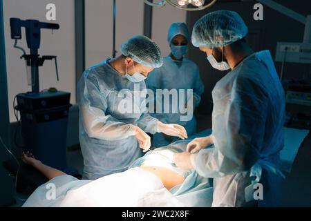 Vue à distance équipe diversifiée de chirurgiens professionnels effectuant la chirurgie invasive sur le patient à l'hôpital. Assistante afro-américaine aidant la tête Banque D'Images