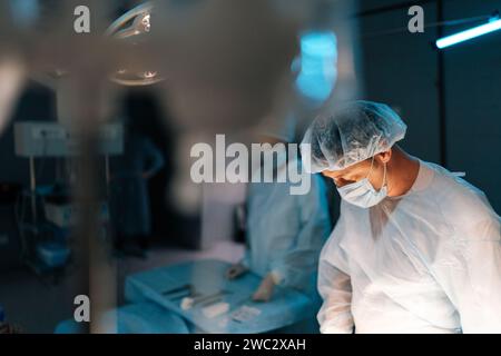 Focalisation sélective de l'équipe coopérante de chirurgiens traitant l'opération chirurgicale dans la salle d'opération sombre service d'urgence moderne de l'hôpital. Banque D'Images