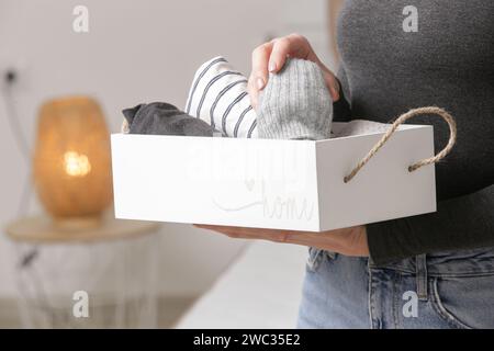 Femme tenant une boîte en bois avec des vêtements chauds, don et concept de charité, vie domestique, organisation et désencombrement. Banque D'Images