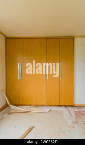 Portes en bois avec poignées en métal de placards intégrés dans la chambre à coucher avec des débris et des déchets sur le sol dans la maison abandonnée Banque D'Images