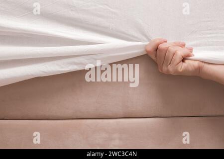 Changer les draps de lit. Femme met un drap de coton blanc ajusté sur un matelas tout en faisant le lit. Banque D'Images