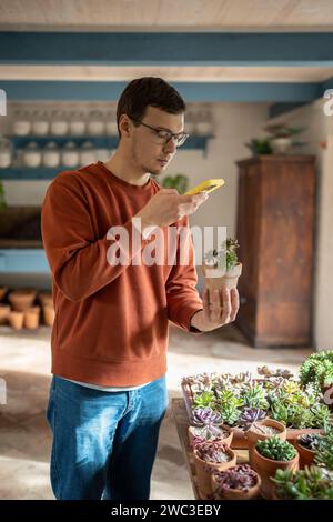 Homme prenant photo de plantes en pot dans le marché floral de magasin sur smartphone. Banque D'Images