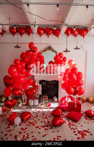 Décoration de chambre chic pour la Saint Valentin. Cheminée près du mur blanc décoré avec des ballons en forme de coeur rouge, sur le sol cadeaux dans des boîtes de vacances, sacs, co Banque D'Images