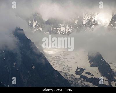 Vue atmosphérique des Alpes italiennes au-dessus de Courmayeur avec un faible soleil perçant les nuages bas sur les sommets enneigés et les rochers Banque D'Images