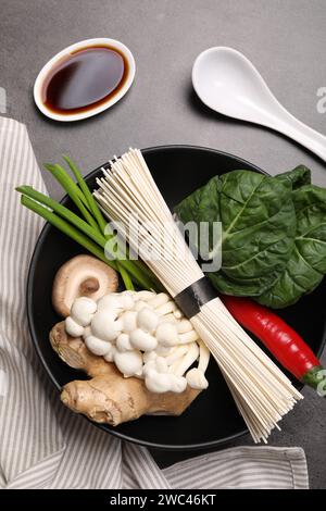 Cuisiner une délicieuse soupe ramen. Différents ingrédients dans des bols et une cuillère sur la table grise, à plat Banque D'Images