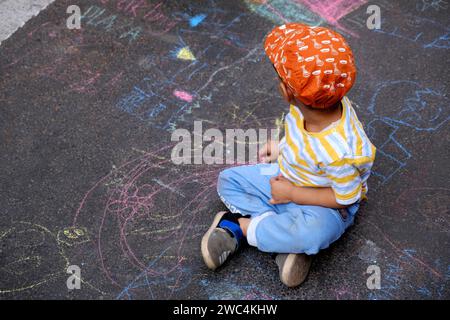 Petit garçon indien dessinant à la craie à l'extérieur. Image des enfants, créativité sur la route grise de dackground, activités extérieures pour les enfants. vue de dessus. Banque D'Images