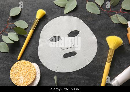 Masque de drap facial avec différents produits cosmétiques et eucalyptus sur fond noir Banque D'Images