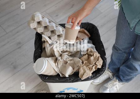 Femme jetant tasse de papier dans la poubelle pleine dans la cuisine, gros plan Banque D'Images