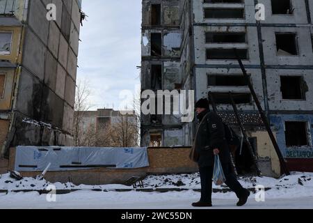 Zaporizhzhia, Ukraine. 13 janvier 2024. Une femme est vue marcher sur la route près de l'immeuble qui a été lourdement endommagé par les bombardements russes à Zaporizhzhia. Le président ukrainien Volodymyr Zelenskiy a déclaré qu’il était plus convaincu aujourd’hui que le mois dernier que son pays obtiendrait une nouvelle aide financière des États-Unis. Mais rien n’indiquait à Washington que l’approbation par le Congrès d’un paquet d’aide proposé par la Maison Blanche serait bientôt disponible. Crédit : SOPA Images Limited/Alamy Live News Banque D'Images