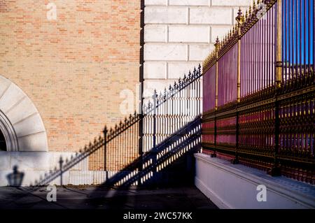 Une grande vieille clôture de couleur magenta avec des montants dorés et des pointes projette une ombre claire sur la façade en briques rouges d'un bâtiment historique. Banque D'Images