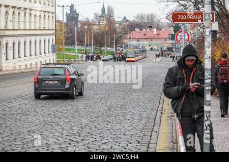 Un sans-abri avec un téléphone dans la rue de la vieille ville médiévale historique de Prague en hiver. Il était concentré et regardait dans le téléphone Banque D'Images