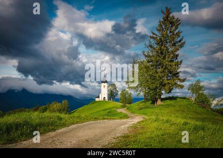 Paysage de printemps rural et petite église sur la crête de la montagne. Superbe vue avec jolie église alpine Saint Primoz en arrière-plan, village de Jamnik, Slovénie Banque D'Images