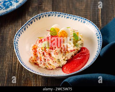 Salade de mayonnaise à la chair de crabe, décorée de mousse de betterave dans une assiette de style restaurant. Salade de crabe imitation avec des bâtons de crabe ou de la chair de crabe et des œufs dans un bol sur fond en bois Banque D'Images