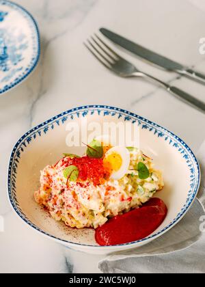 Salade de mayonnaise à la chair de crabe, décorée de mousse de betterave dans une assiette de style restaurant. Salade de crabe imitation avec des bâtons de crabe ou de la viande et des œufs dans un bol sur fond de marbre. Vertical, Copyspace Banque D'Images