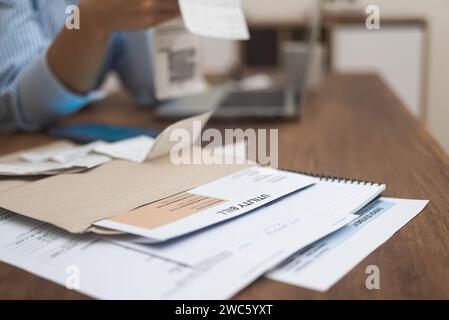 Factures de services publics, indiquant le montant dû, sur une table en bois femme examine ses documents bancaires. Banque D'Images
