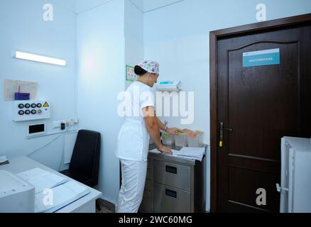 En service. L'infirmière se tient à un poste d'infirmière en train de chercher dans les cartes des patients. Clinique régionale 1. Kiev, Ukraine Banque D'Images