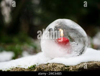 Lanterne globe de glace avec bougie rouge brûlant à l'intérieur dans le jardin du soir. Artisanat d'hiver et art de glace ou concept de décoration extérieure. Banque D'Images