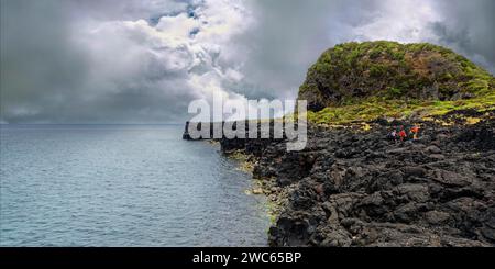 Groupe de personnes marchant le long d'une côte rocheuse avec un ciel nuageux au-dessus, rochers de lave sentier côtier Ponta da Iiha, Calhau, côte ouest, Pico, Açores Banque D'Images