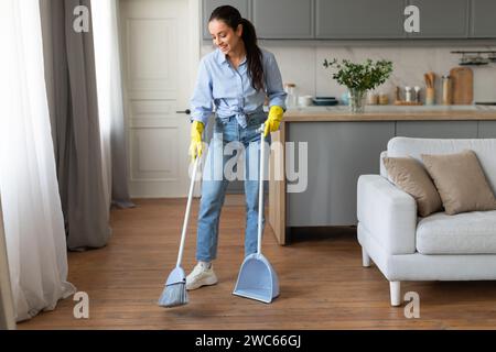 Femme avec balai et pelle nettoyant le plancher en bois Banque D'Images