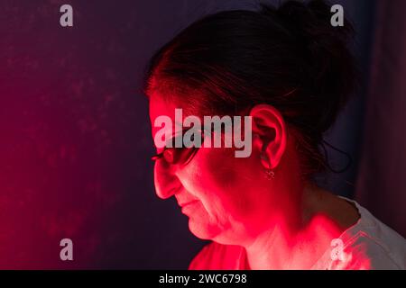 Gros plan du visage de femme senior faisant la séance de thérapie à la lumière rouge avec panneau et portant une protection oculaire Banque D'Images
