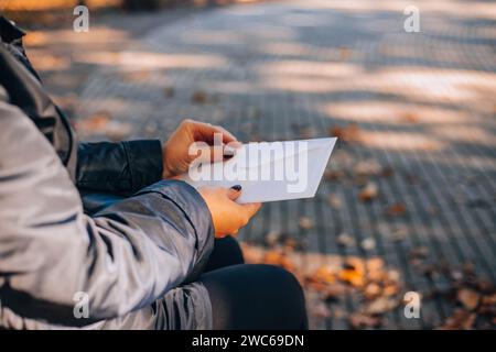 Femme ouvre une enveloppe blanche avec une lettre. Feuillage d'automne en arrière-plan. Banque D'Images
