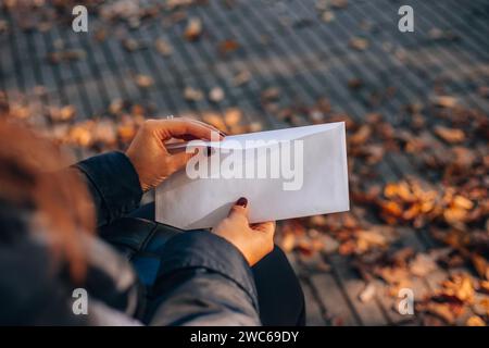 Femme ouvre une enveloppe blanche avec une lettre. Feuillage d'automne en arrière-plan. Banque D'Images