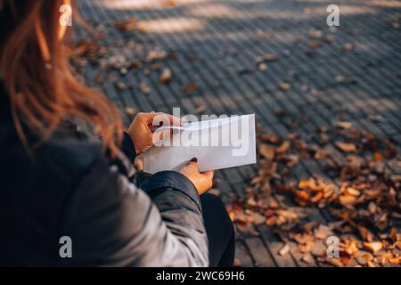 Femme ouvre une enveloppe blanche avec une lettre. Feuillage d'automne en arrière-plan. Banque D'Images