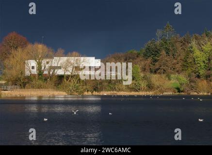 Lurgan Park, Lurgan, comté d'Armagh, Irlande du Nord, Royaume-Uni. 14 janvier 2024. Météo britannique - un dimanche matin froid avec soleil et averses au parc Lurgan. Soleil d'hiver reflétant le dos du club de golf Lurgan Club avec un fond de nuages sombres au-dessus du lac du parc. Crédit : CAZIMB/Alamy Live News. Banque D'Images