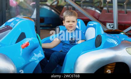 Petit garçon s'amusant à monter une grosse voiture pare-chocs bleue. Banque D'Images