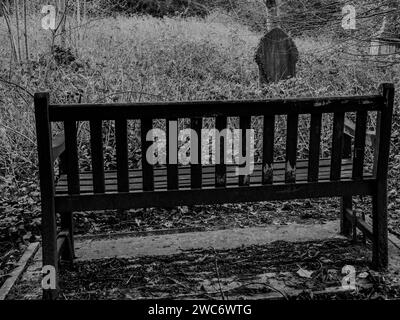 Banc vide et solitaire regardant vers une pierre tombale dans un cimetière à Cardiff, pays de Galles. Pierres tombales. Évocateur, triste, pleuré, gothique, mort, au-delà Banque D'Images