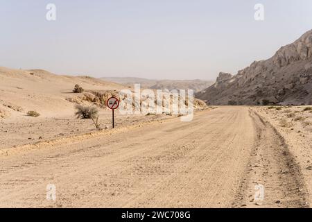 Paysage avec panneau routier sans dépassement sur route de gravier dans le désert de Moonlandscape , tourné dans la lumière brillante de la fin du printemps près de Swakopmund, Namibie, Afrique Banque D'Images