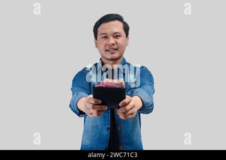Jeune homme asiatique montrant l'expression heureuse du visage tout en tenant son portefeuille plein d'argent Banque D'Images